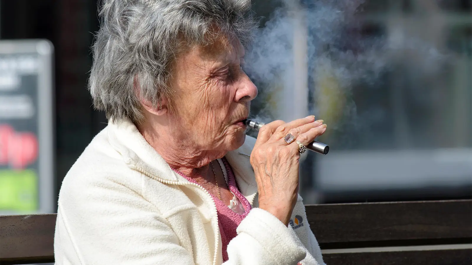 Woman with grey hair holding a vaping device to her lips and inhaling.